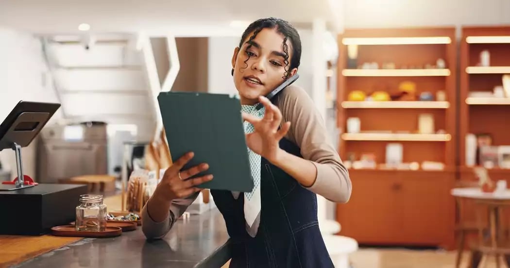 An employee in an apron making a call while doing restaurant inventory management on a tablet.