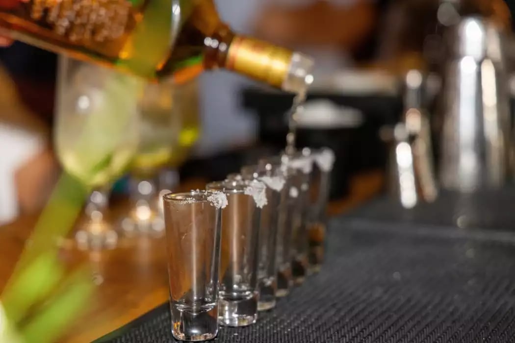 A close-up photo of a bartender’s hand pouring a row of shots.